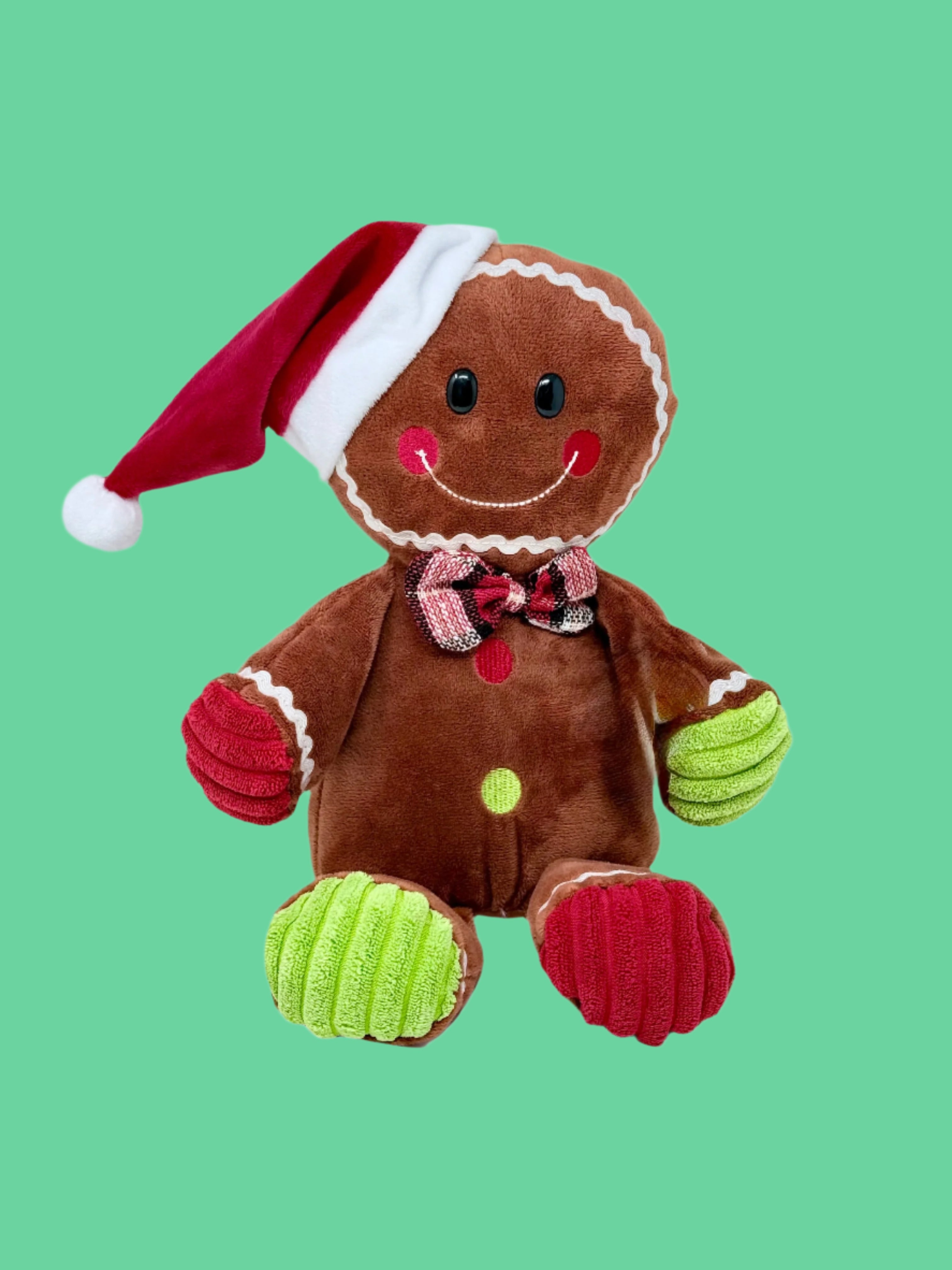 A plush toy resembling a gingerbread man with a red and green hat, brown 'ginger' body, and green 'icing' accents on the hands and a red scarf.
